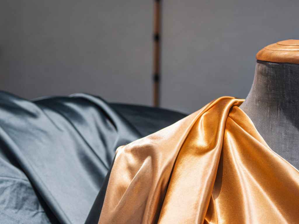Draped gold satin fabric on dress form with dark background