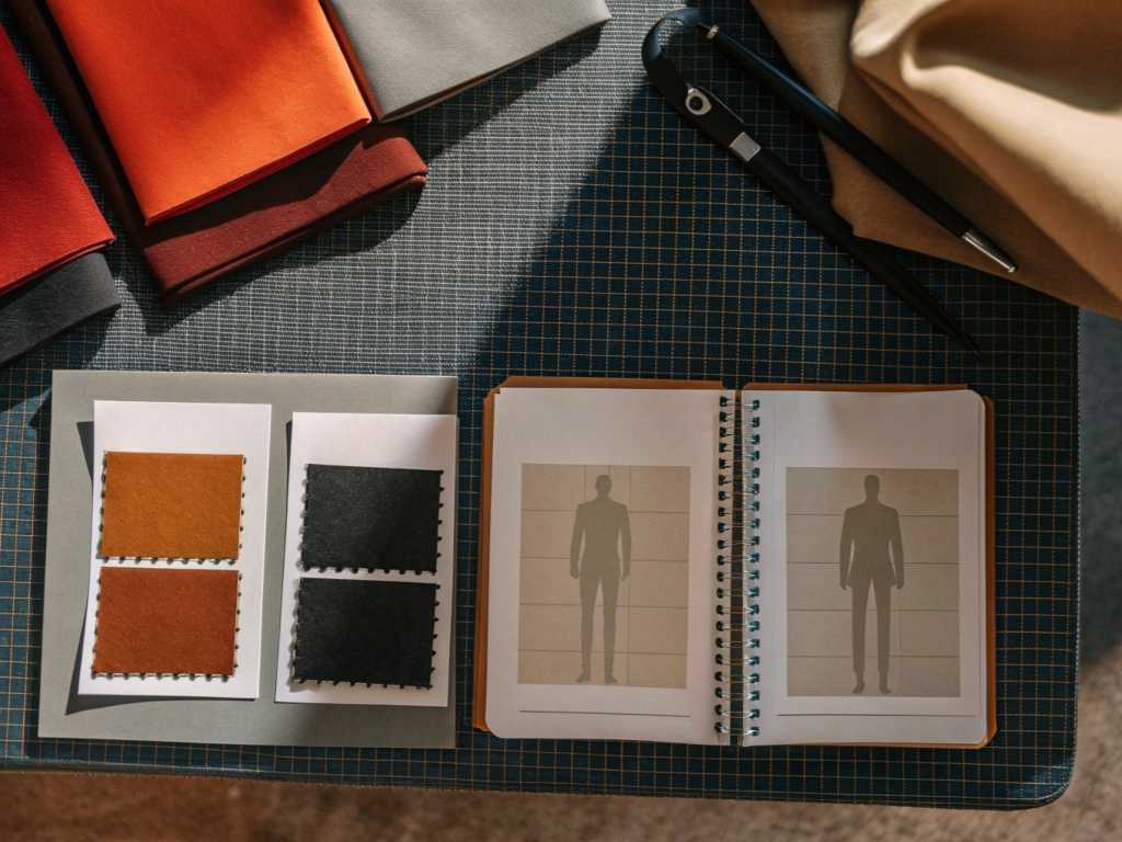 Fabric swatches and fashion design notebook placed on designer workspace.