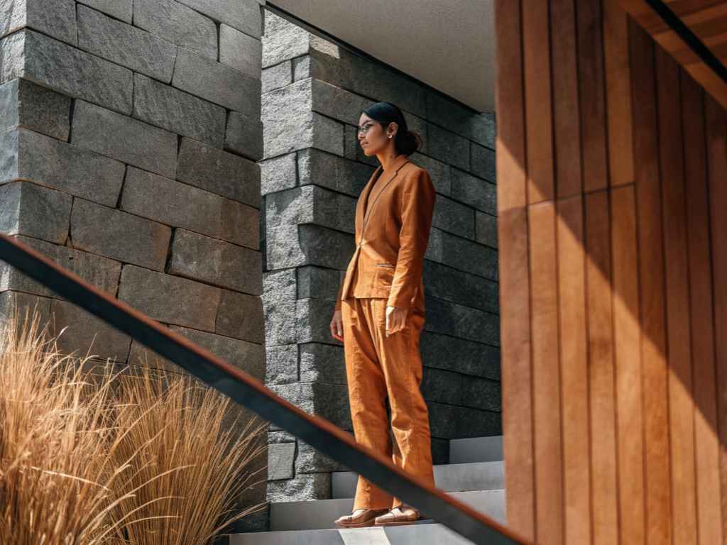 Woman in rust-colored suit standing near stone wall