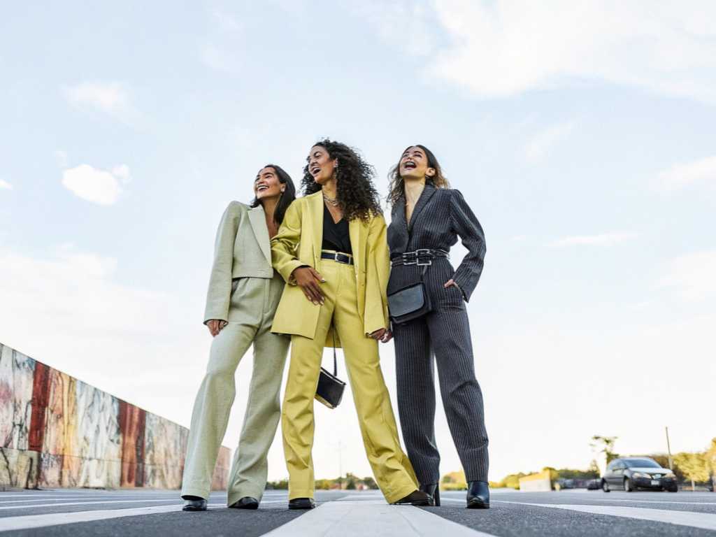 Three stylish women in colorful power suits standing confidently on city crosswalk