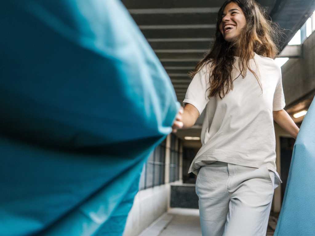 Woman smiling in casual beige outfit pulling blue fabric indoors