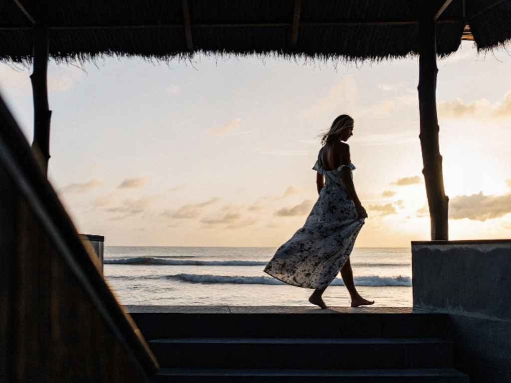 Woman in flowing dress walking near beach at sunset