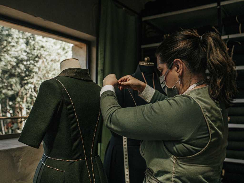 Seamstress measuring green dress on mannequin in tailoring studio