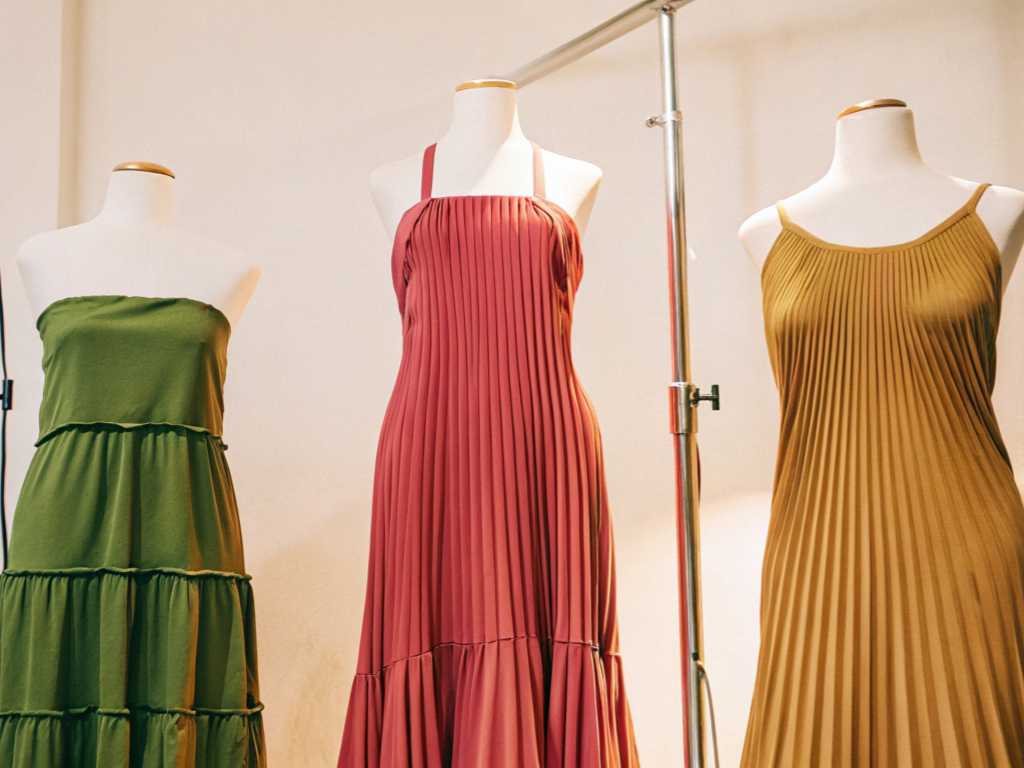Three colorful pleated and tiered dresses displayed on white mannequins