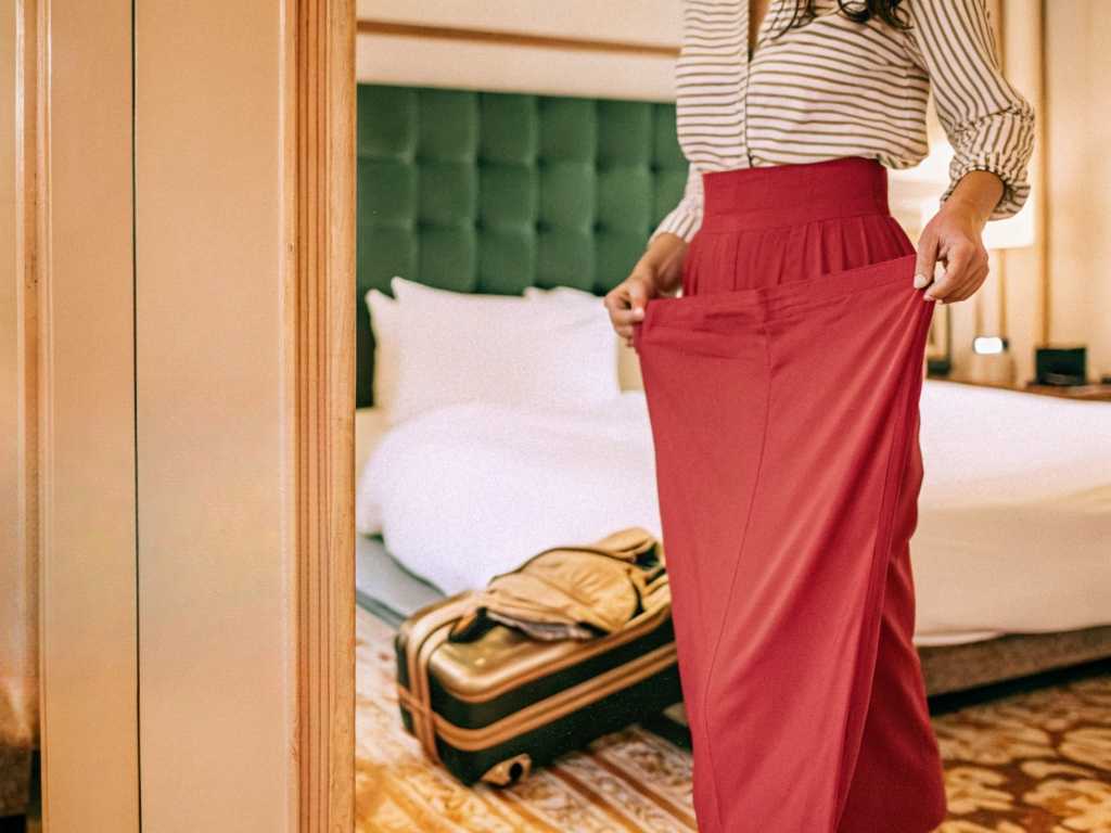 Woman trying on elegant red skirt in hotel room.