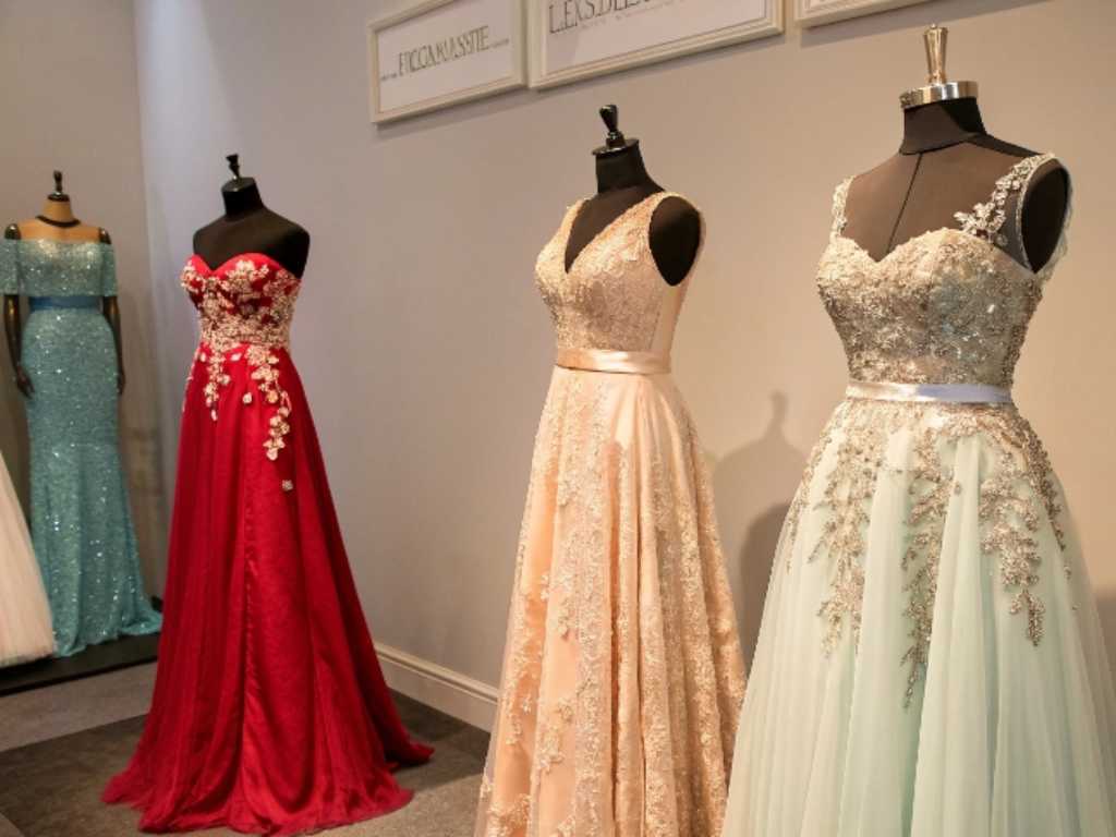 Elegant evening gowns with lace and embroidery displayed on mannequins.