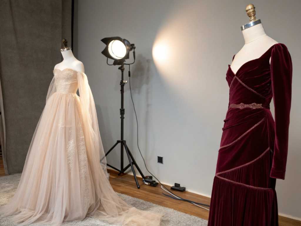 Two elegant gowns on mannequins in a fashion studio with spotlight.